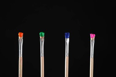 Siyah arkaplanda renk boyalı birçok fırça, yakın plan