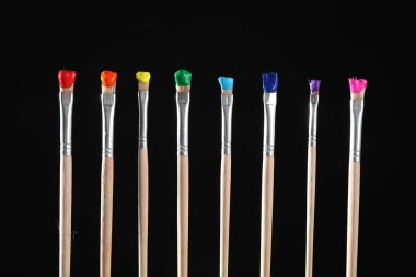 Siyah arkaplanda renk boyalı birçok fırça, yakın plan