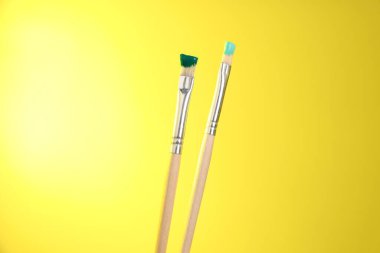 Sarı arkaplanda renkli iki fırça, yakın plan.