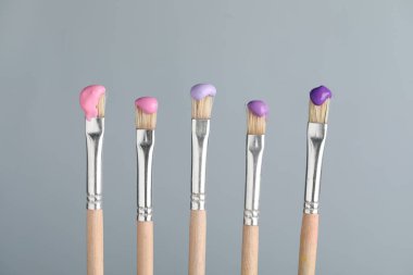 Açık gri arkaplanda renk boyalı pek çok fırça, yakın plan