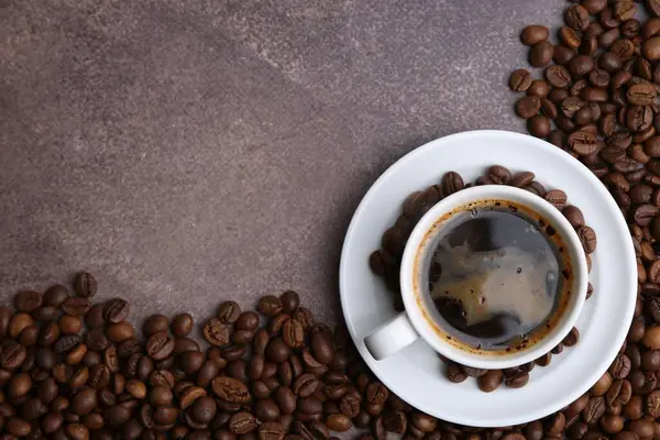 Aromatik kahve fincanda, fincan tabağı ve kahve çekirdekleri kahverengi desenli masada, düz yerde. Metin için boşluk