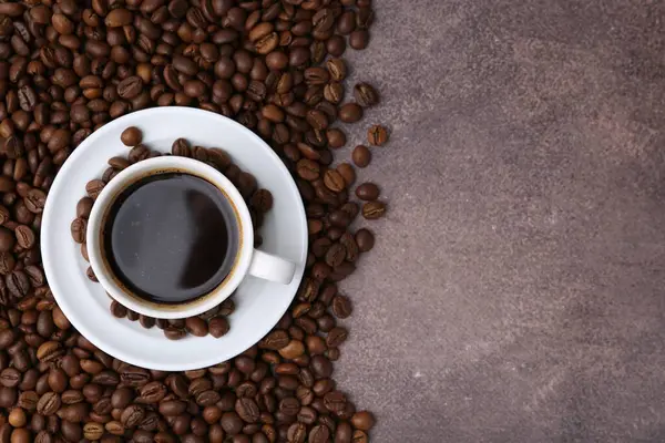 Aromatik kahve fincanda, fincan tabağı ve kahve çekirdekleri kahverengi desenli masada, düz yerde. Metin için boşluk