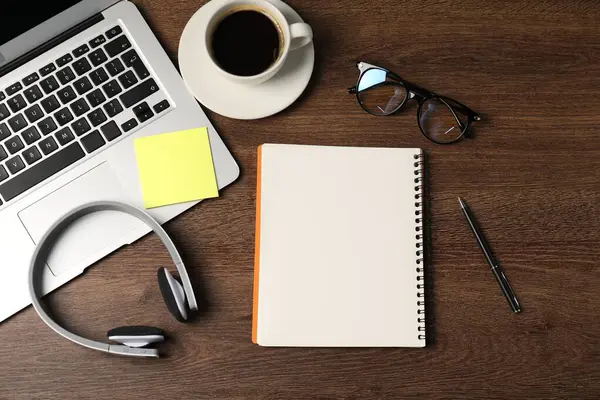 Not defteri, yapışkan not, kalem, kulaklık, kahve ve dizüstü bilgisayar ahşap masaya, düz uzan.