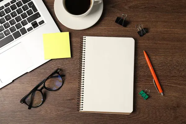 Not defteri, kalem, yapışkan not, cilt klipsleri, bardaklar, kahve ve dizüstü bilgisayar ahşap masa, düz uzanma