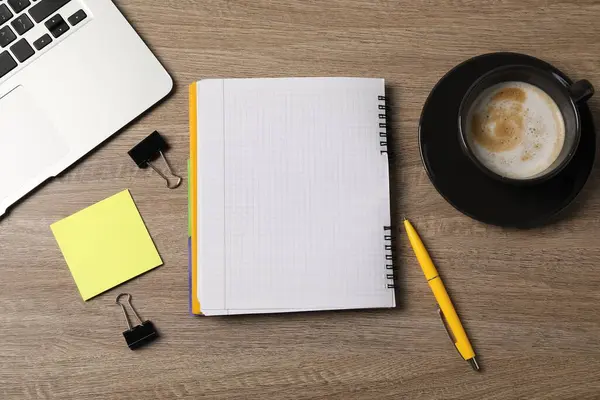 Not defteri, yapışkan not, kalem, cilt klipsleri, ahşap masaya kahve ve dizüstü bilgisayar.