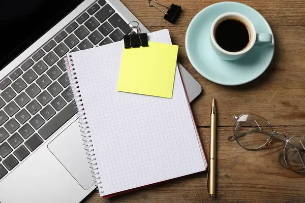 Kalemli defter, yapışkan not, dizüstü bilgisayar, ataç ve ahşap sehpada kahve.