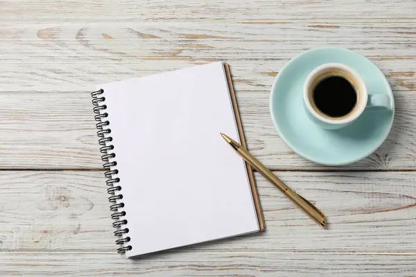 Beyaz ahşap masa üzerinde kalem ve kahve bulunan defter, üst manzara.