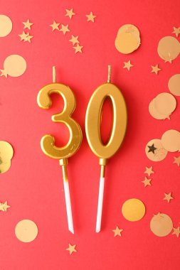 30th birthday. Number shaped candles and confetti on red background, flat lay