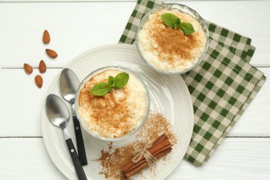 Tarçınlı, nane, badem ve kaşıklı lezzetli sütlaç beyaz ahşap masa, düz uzanmış