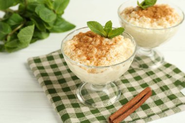 Tarçınlı lezzetli pirinç pudingi ve beyaz ahşap masadaki cam tatlı kaseleri, yakın plan.