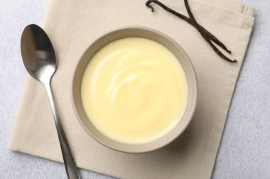 Lezzetli vanilyalı puding kasede, kapsüller ve kaşık açık gri masada, düz yerde