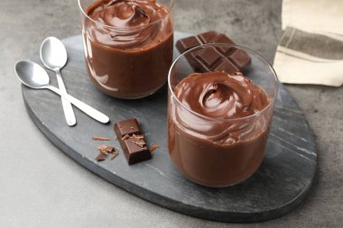 Lezzetli puding ve çikolata parçaları gri masada, yakın plan.