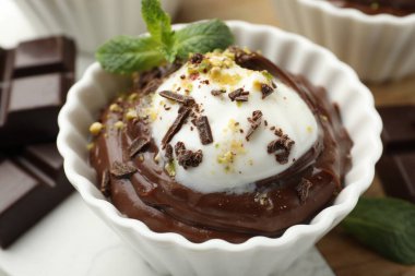 Lezzetli puding, krema kasesinde ve çikolata parçaları masada, yakın plan.