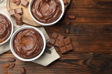 Tabaklardaki lezzetli pudingler, çikolata parçaları ve kakao çekirdekleri ahşap masada, düz bir şekilde. Metin için boşluk