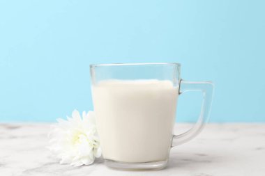 Beyaz mermer masada açık mavi arka planda bir fincan süt ve çiçek.