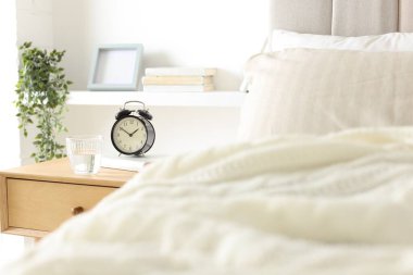 Alarmlı komodinli komodin, bir bardak su ve yatağın yanında kitap.