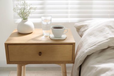 Komodinin yanında bir bardak su, vazoda çiçekler ve yatağın yanında kahve, yakın plan.