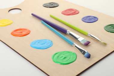 Beyaz arka planda boya ve fırçalı ahşap palet, yakın plan.