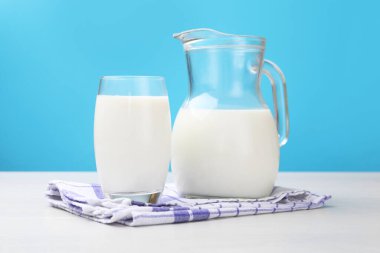 Bardakta taze süt ve açık mavi arka planda beyaz ahşap masada sürahi.