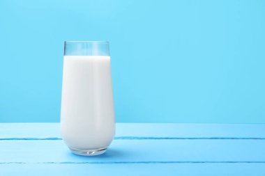 Açık mavi ahşap masada cam içinde taze süt. Metin için boşluk