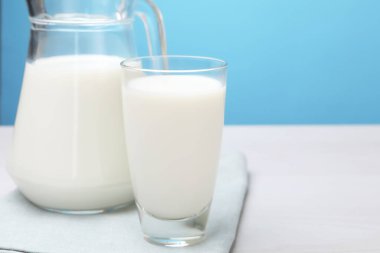 Bardakta taze süt ve beyaz ahşap masada açık mavi arka planda sürahi, yakın plan. Metin için boşluk