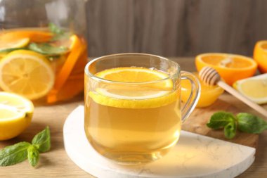 Cam fincanda aromatik meyve çayı, portakal, limon, bal ve nane, ahşap masada, yakın plan.
