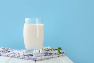 Bardaktaki taze süt ve beyaz ahşap masadaki çiçekler açık mavi arka planda, yakın plan.