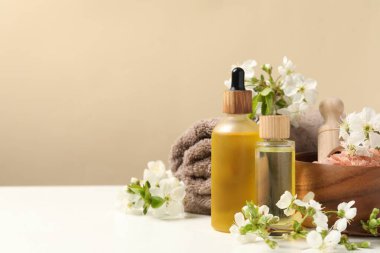 Beyaz masa üzerinde kozmetik ürünleri ve güzel çiçeklerle bej arkaplan, metin için boşluk