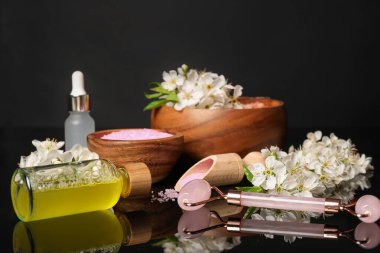 Siyah ayna yüzeyinde kozmetik ürünleri ve güzel çiçeklerle kaplıca kompozisyonu, yakın plan.