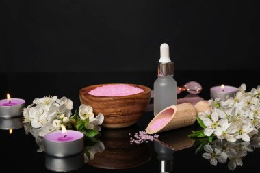 Kozmetik ürünleriyle kaplıca kompozisyonu, yanan mumlar ve siyah ayna yüzeyinde güzel çiçekler, yakın plan.