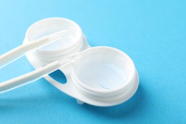 Açık mavi arkaplanda kontak lensler ve cımbızlar, yakın plan