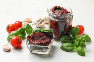 Lezzetli güneşte kurutulmuş domatesler, taze sebzeler, fesleğen ve sarımsak beyaz masada, yakın plan.