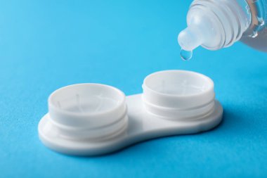 Açık mavi arka planda kontakt lensleri olan çözeltiye damlatılıyor, yakın plan. Metin için boşluk