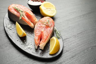 Deniz ürünleri. Siyah desenli masada somon biftekleri, baharatlar ve limon dilimleri, yakın plan. Metin için boşluk