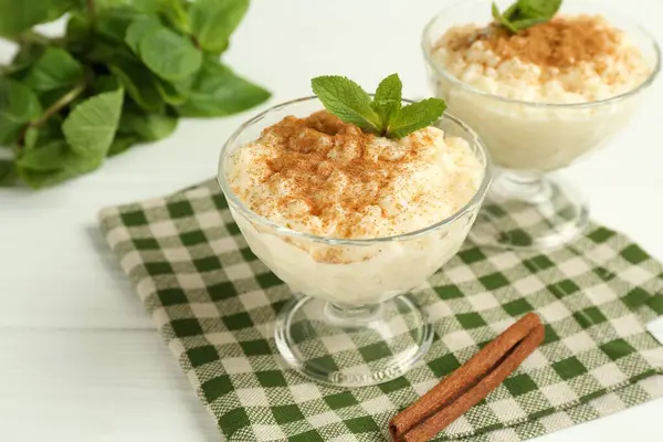 Tarçınlı lezzetli pirinç pudingi ve beyaz ahşap masadaki cam tatlı kaseleri, yakın plan.