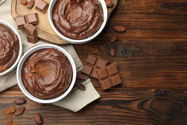 Tabaklardaki lezzetli pudingler, çikolata parçaları ve kakao çekirdekleri ahşap masada, düz bir şekilde. Metin için boşluk