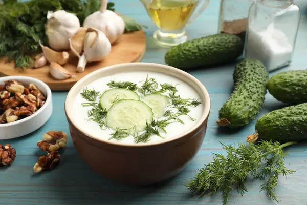 Açık mavi ahşap masadaki ürünler arasında dereotlu lezzetli salatalık çorbası, yakın plan.