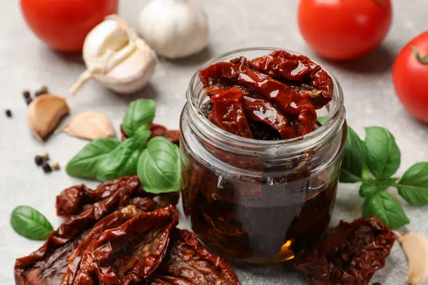 Lezzetli güneşte kurutulmuş domatesler, taze sebzeler ve baharatlar gri masada, yakın plan.