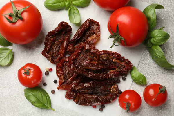 Lezzetli güneşte kurutulmuş domatesler, taze sebzeler ve baharatlar gri desenli masada, düz yerde.