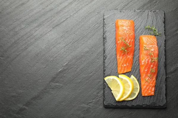 Deniz ürünleri. Somon fileto parçaları, kekik ve limon dilimleri siyah desenli masa, üst manzara. Metin için boşluk