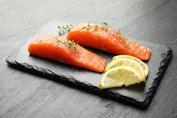 Deniz ürünleri. Somon fileto parçaları, kekik ve limon dilimleri siyah desenli masa, yakın plan.