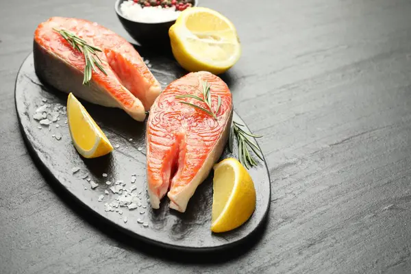 Deniz ürünleri. Siyah desenli masada somon biftekleri, baharatlar ve limon dilimleri, yakın plan. Metin için boşluk