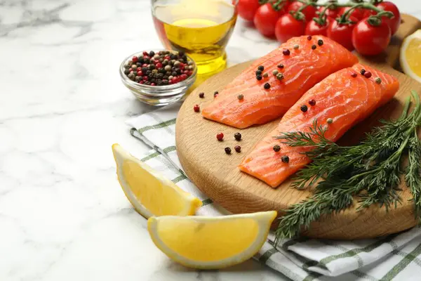 Deniz ürünleri. Somon fileto, domates, yağ, baharat ve limon dilimleri beyaz mermer masada, yakın plan.