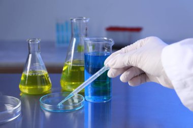 Bilim adamı, laboratuardaki masada petri kabından pipetle numune alıyor, yakın plan.