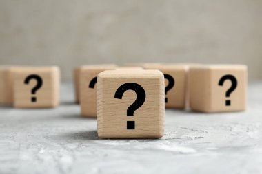 Gri desenli masa üzerinde soru işaretleri olan tahta küpleri, yakın plan.