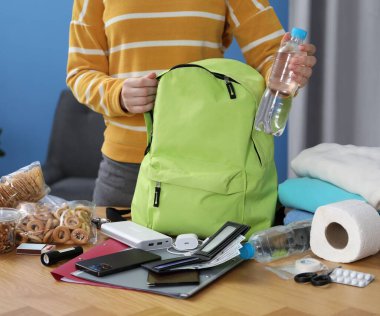 Hayatta kalma kiti. Kadın, ahşap masada sırt çantasına farklı acil durum malzemeleri yerleştiriyor.