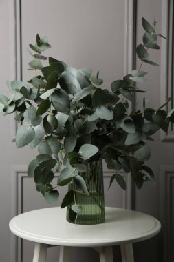 Gri duvarın yanındaki masada vazoda okaliptüs dalları var.