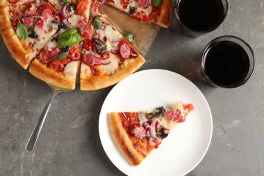 Gri masada servis edilen ince tütsülenmiş sosisli lezzetli bir pizza.