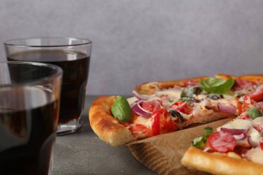 İnce füme sosisli lezzetli pizza ve gri masada soda, yakın plan.