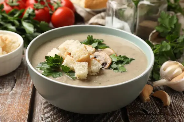 Lezzetli mantar kremalı çorba ve ahşap masada malzemeler, yakın plan.